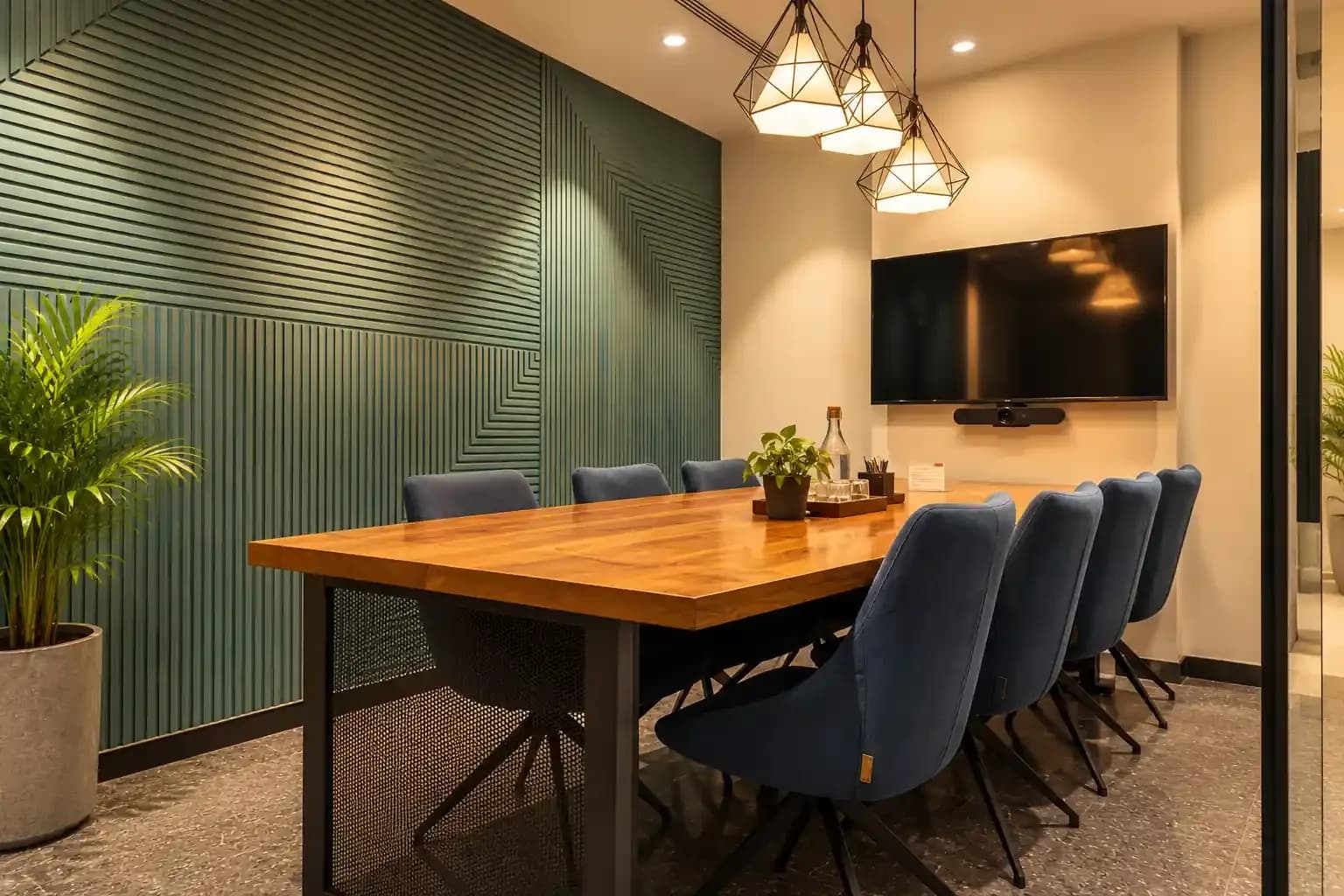 ClayWorks meeting room with a wooden table, navy chairs, pendant lights and a green slatted wall